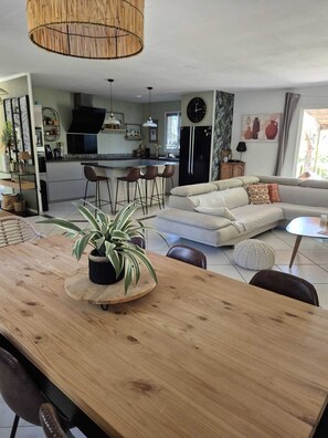 Eine moderne Küche mit einer Kochinsel, ein Essbereich mit einem Holztisch und Stühlen sowie eine Wohnbereich mit einer Couch und Kissen.
