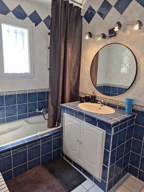 Un baño con bañera, lavamanos, espejo y azulejos azules.