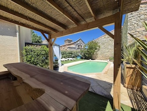 Una pérgola de madera con una piscina y un edificio de piedra al fondo.