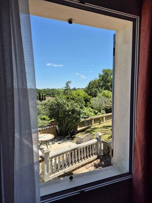 Ein Balkon mit Blick auf einen Garten, eine Steinbalustrade und einen strahlend blauen Himmel.