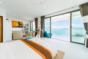 Ein modernes Hotelzimmer mit einem großen Bett, einer Sitzecke, einem Bücherregal und Meerblick.