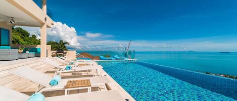 Uma área na piscina com espreguiçadeiras, vista clara do oceano e cenário tropical.