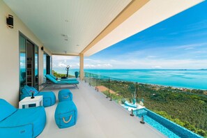 Ein Balkon mit blauen Sitzkissen, einer Glastrennwand und Blick auf das Meer und die Landschaft.