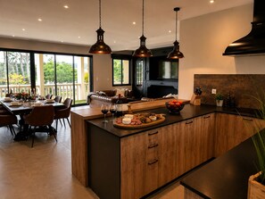 A modern kitchen with wooden cabinetry, a central island, pendant lighting, and a dining area with a view. - Le Chesterfield - 4 suites with private Jacuzzi at Domaine de Giverzac (Domme)