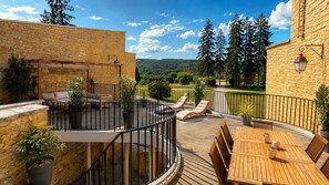 A stone building with a wooden deck, outdoor seating, and a view of the surrounding landscape. - Le Chesterfield - 4 suites with private Jacuzzi at Domaine de Giverzac (Domme)