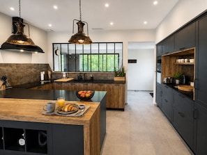 A modern kitchen with a central island, dark cabinetry, and pendant lighting. - Le Chesterfield - 4 suites with private Jacuzzi at Domaine de Giverzac (Domme)