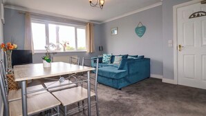 Un salon avec un canapé bleu, une table à manger avec des chaises, un téléviseur et un lustre.
