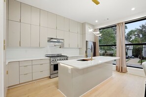 A modern kitchen with a central island, stainless steel appliances, and a large window with a view of the outdoors. - Custom Luxury Townhome in the Heart of Midtown 3Bed/3.5Bath Sleeps 6 (Atlanta)