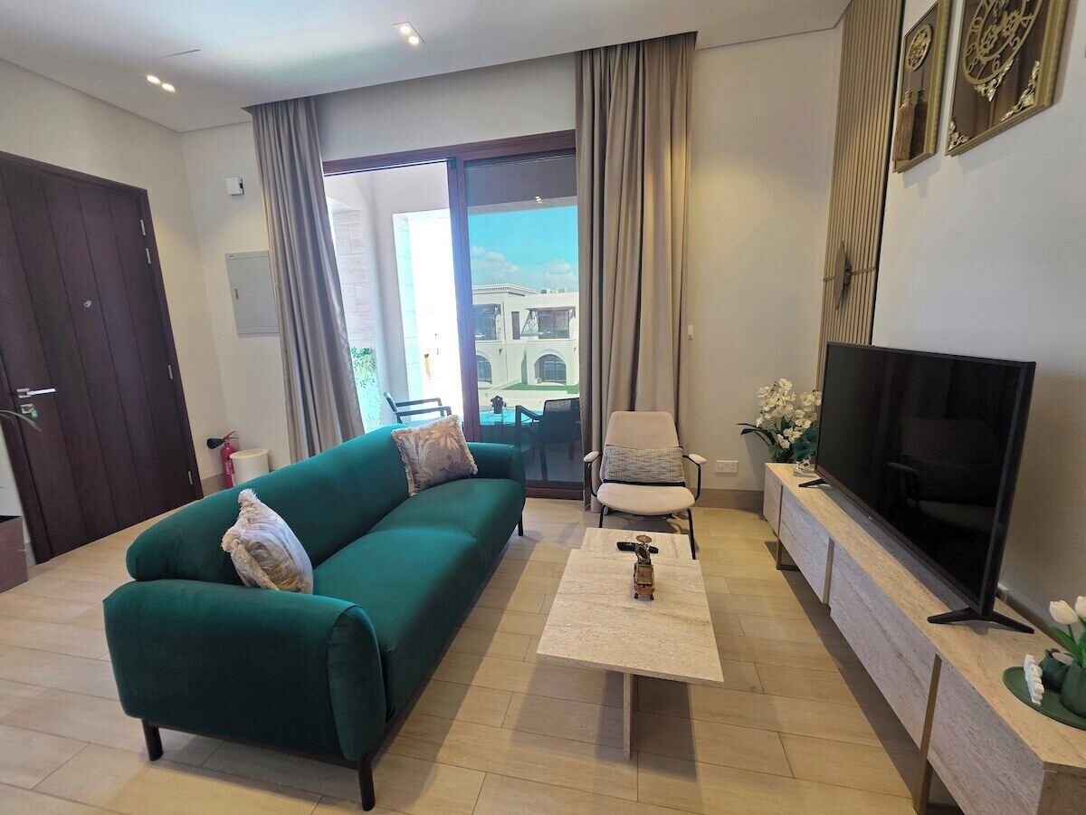 A living room with a sofa, a chair, a coffee table, a TV, and a sliding glass door leading to an outdoor area.