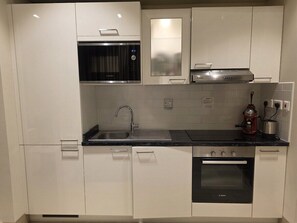 Uma cozinha moderna com armários brancos, uma pia de aço inoxidável, um forno Bosch e um micro-ondas.