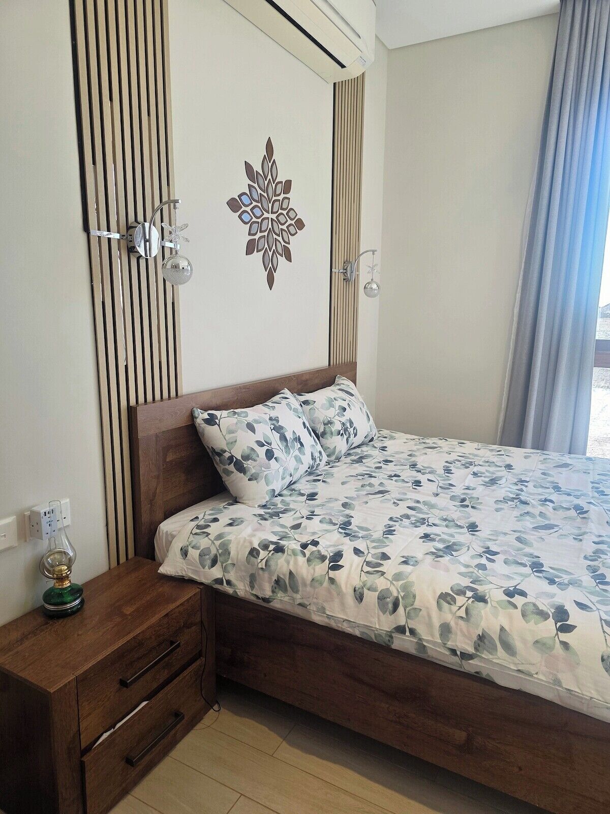 Un dormitorio con cama de madera, mesita de noche, lámpara de pared y un adorno mural.