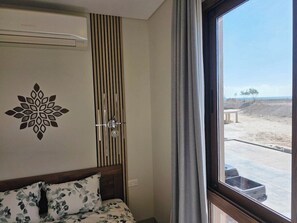 Ein Zimmer mit einem Bett, einem Kleiderschrank, einem Fenster mit Blick auf eine Wüstenlandschaft und einer Wand-Klimaanlage.