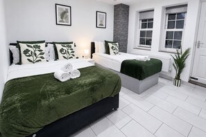 Ein Hotelzimmer mit zwei Betten, Bettwäsche in Grün und Weiß, einer grauen Bank, einer Topfpflanze und gerahmten Bildern an den Wänden.