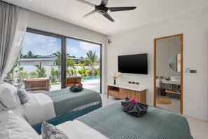 Ein modernes Hotelzimmer mit einem großen Bett, einem Fernseher, einem Badezimmer und einem Balkon mit Pflanzen.