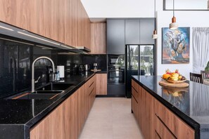 Eine moderne Küche mit Holzausziehtüren, schwarzen Arbeitsplatten und einer zentralen Kochinsel mit Obst.