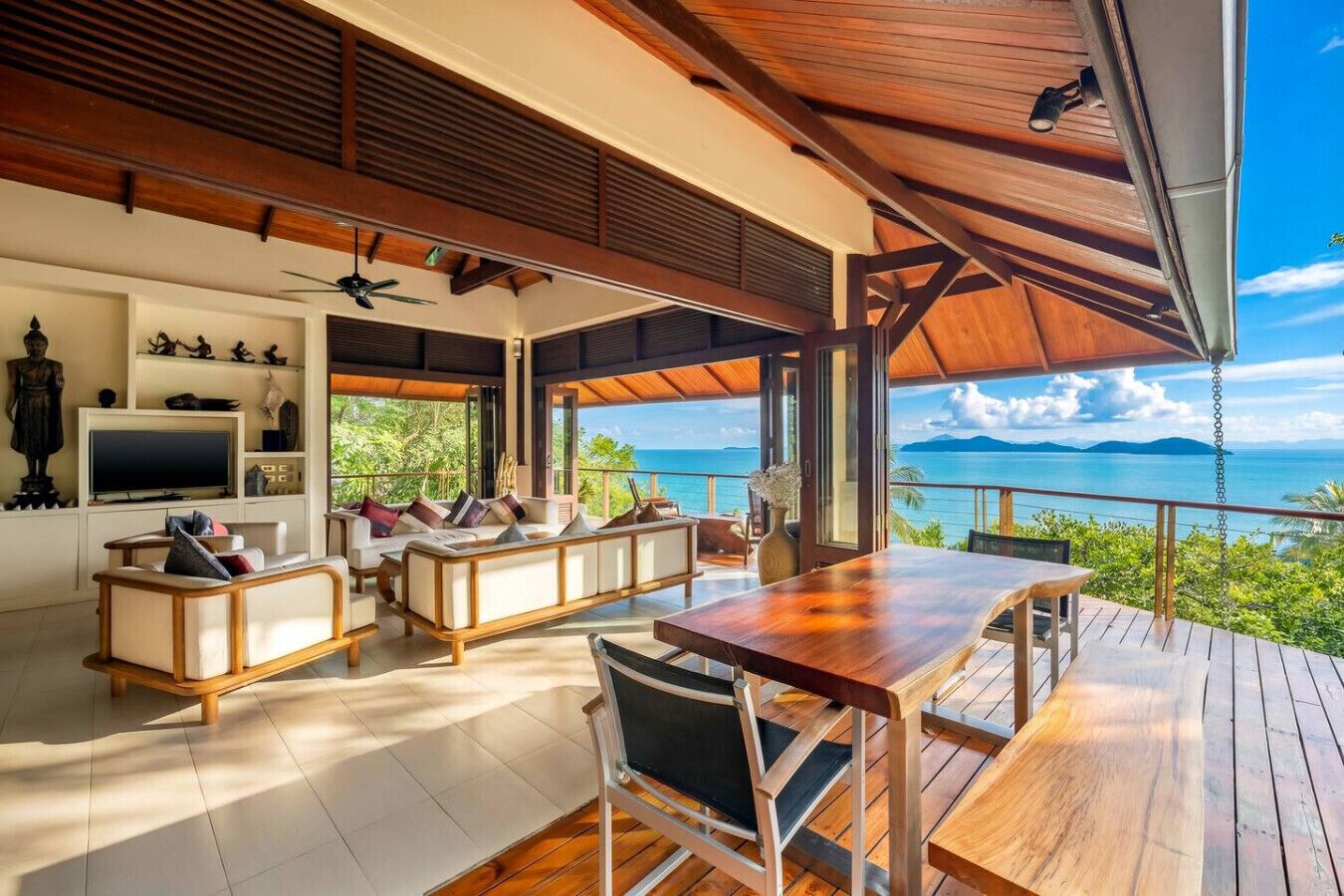 Un vaste espace de vie extérieur doté d’une terrasse en bois, d’une table à manger et d’un ensemble de canapés.