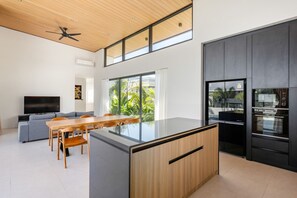 Eine moderne Küche mit einer großen Kochinsel, einem Essbereich mit Holztisch und -stühlen, einem eingebauten Fernseher und einem Deckenventilator.