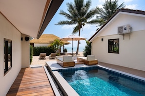 Ein Poolbereich mit Liegestühlen, einer Struktur mit Reetdach und einer Palme.