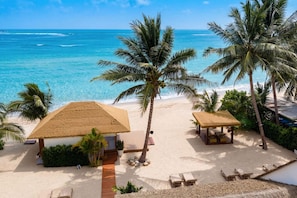 Ein Strand mit strohgedeckten Hütten, Palmen und freiem Blick auf das Meer.