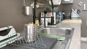 Et moderne køkken med vask i rustfrit stål, et opvaskestativ og en elkedel.
