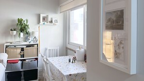 Et kompakt køkken med spisebord, hvide stole og et vindue med persienner.