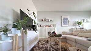 En stue med et fladskærms-tv, en sofa, et sofabord og en lurvet måtte.