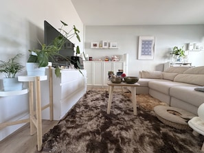 Ein Wohnzimmer mit Flachbildfernseher, einer Couch, einem Couchtisch und einem flauschigen Teppich.