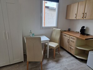 Une petite cuisine Ă©quipĂ©e avec une table blanche, une chaise, une fenĂȘtre et des placards en bois.