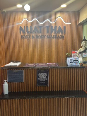 A reception desk with a wooden panel design, a Nuat Thai Foot & Body Massage sign, a statue, and a QR code for mobile scanning. - Family Condo SMB Live,Love & Laugh & have Fun (Pasay City)