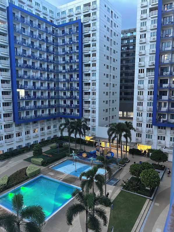 A high-rise residential building with multiple balconies, a swimming pool, and landscaped areas. - Family Condo SMB Live,Love & Laugh & have Fun (Pasay City)