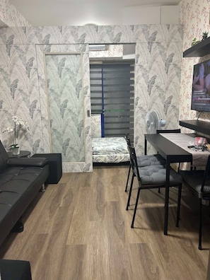 A compact living space with a sofa, a dining table with chairs, a TV, and a sliding door leading to a balcony. - Family Condo SMB Live,Love & Laugh & have Fun (Pasay City)