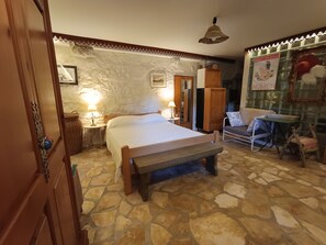 A room with a stone floor, a bed with a wooden headboard, a small table, a chair, and a wall with a 'WOMEN' sign. - Welcome to our charming, authentic stone house on the island of Krk. (Kornić)