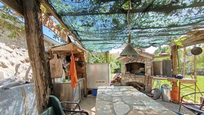 An outdoor kitchen area with a stone table, a pizza oven, and a hanging light fixture. - Welcome to our charming, authentic stone house on the island of Krk. (Kornić)
