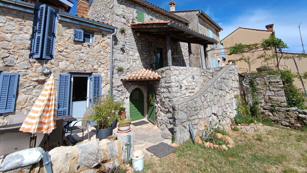 A stone house with a green door, shutters, and a small patio with outdoor furniture and plants. - Welcome to our charming, authentic stone house on the island of Krk. (Kornić)