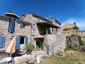A stone house with a green door, shutters, and a small patio with outdoor furniture and plants. - Welcome to our charming, authentic stone house on the island of Krk. (Kornić)