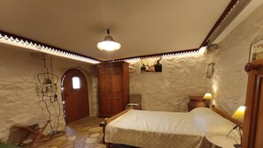 A bedroom with a bed, a wooden wardrobe, a small table, a chair, and a stone-patterned floor. - Welcome to our charming, authentic stone house on the island of Krk. (Kornić)