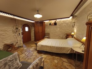 A bedroom with a bed, a wooden wardrobe, a small table, a chair, and a stone-patterned floor. - Welcome to our charming, authentic stone house on the island of Krk. (Kornić)