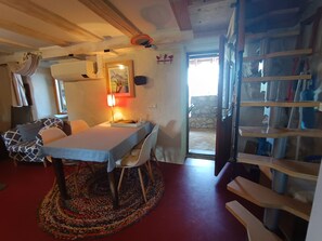 Et hyggeligt rum med et spisebord, stole, et mønstret tæppe, en lampe og en trappe.