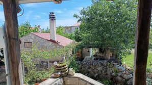 A stone-built outdoor area with a wooden pergola, stone steps, and a view of a house with a red roof. - Welcome to our charming, authentic stone house on the island of Krk. (Kornić)