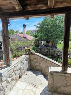 A stone-built outdoor area with a wooden pergola, stone steps, and a view of a house with a red roof. - Welcome to our charming, authentic stone house on the island of Krk. (Kornić)
