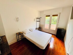 Une chambre à coucher avec un lit, une petite table, un radiateur, une fenêtre donnant sur un beau paysage et un haut-parleur noir.