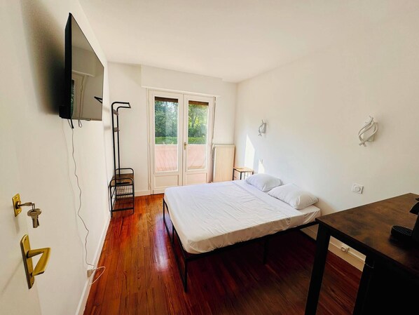 Une chambre avec un lit, un téléviseur fixé au mur, une porte avec une clé et une fenêtre donnant sur un paysage verdoyant.
