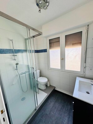 Une salle de bain avec une douche à parois de verre, des toilettes, une fenêtre et un lavabo.