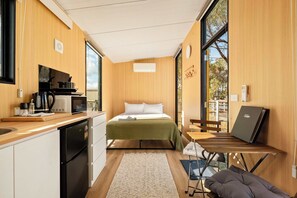 A compact room with a bed, kitchenette, and a small table with a laptop.