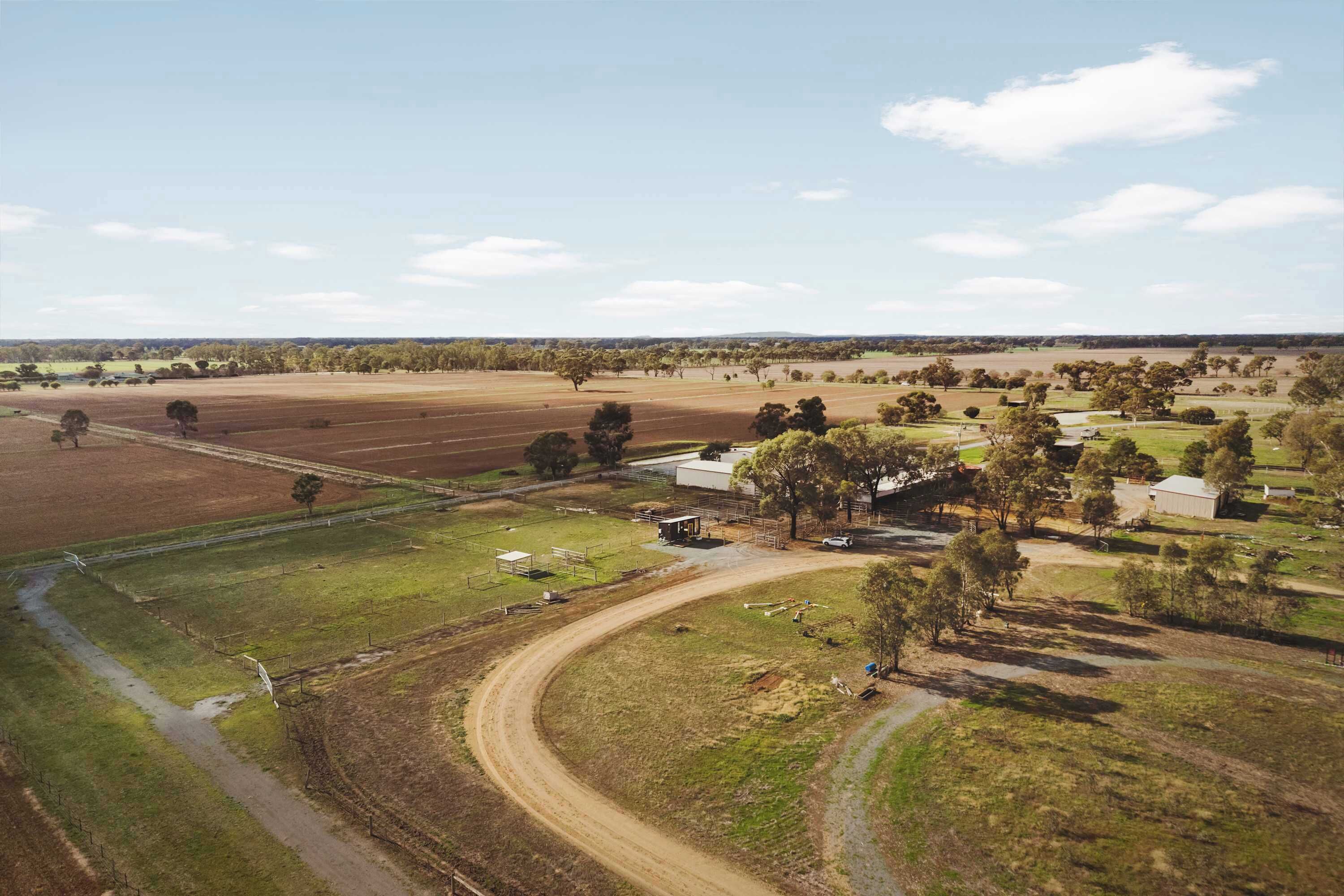 Une vue aérienne d’un paysage rural, avec des champs, un chemin de terre et quelques bâtiments dispersés.