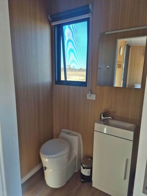 A compact bathroom with a toilet, sink, and window. - Kookaburra Retreat by Tiny Away (Arcadia)