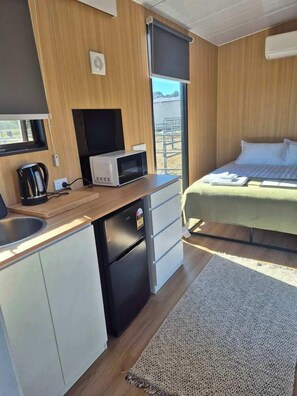 A compact room with a kitchenette, a bed, and a view of the outside. - Kookaburra Retreat by Tiny Away (Arcadia)