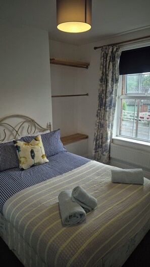 A neatly made bed with a striped bedspread, pillows with floral patterns, and a rolled towel on the bed. - Cool, Calm Georgian Apartment base in Shrewsbury -pet friendly (Shrewsbury)