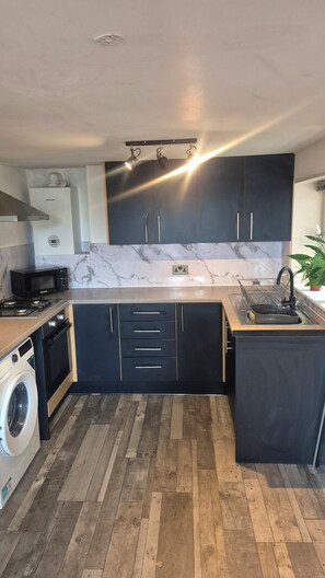 A modern kitchen with dark cabinetry, a built-in washing machine, a microwave, and a sink with a dish rack. - Cool, Calm Georgian Apartment base in Shrewsbury -pet friendly (Shrewsbury)