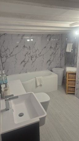 A modern bathroom with a marble wall, a bathtub, a sink, and a small wicker basket.. Cool, Calm Georgian Apartment base in Shrewsbury -pet friendly